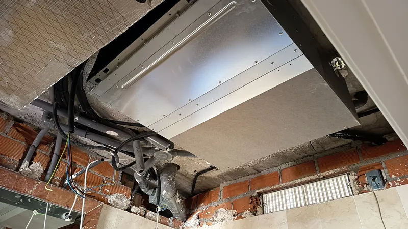Unidad interior de conductos vista desde debajo, con la rejilla de retorno y el hueco del falso techo