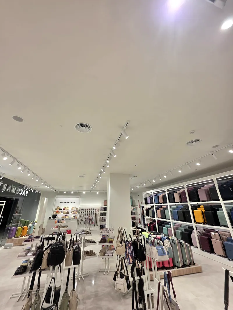 Interior de una tienda de bolsos y complementos climatizada por conductos, con las rejillas integradas en el falso techo
